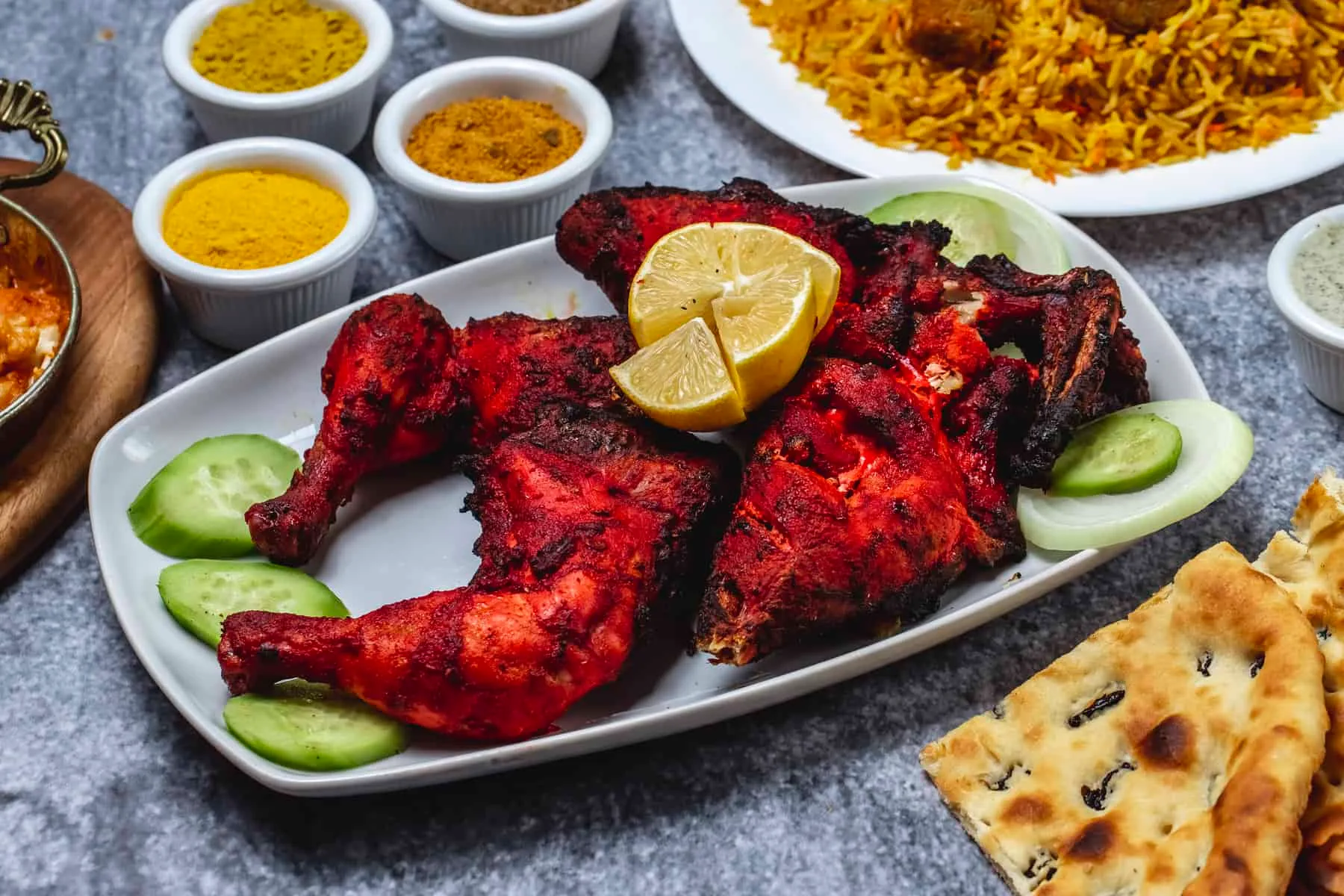 Tandoori chicken served with cucumber, lemon and naan bread on a table