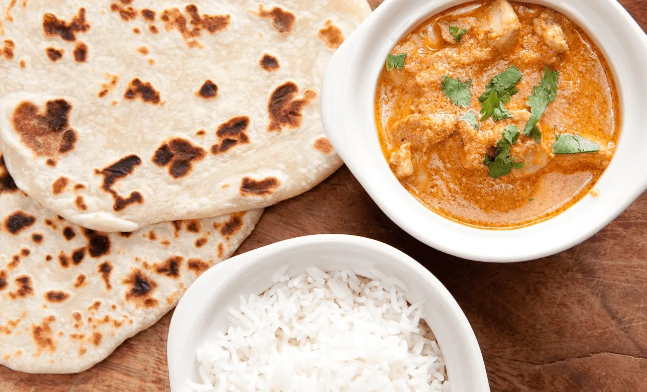 Indian curry served with roti and rice on a wooden table